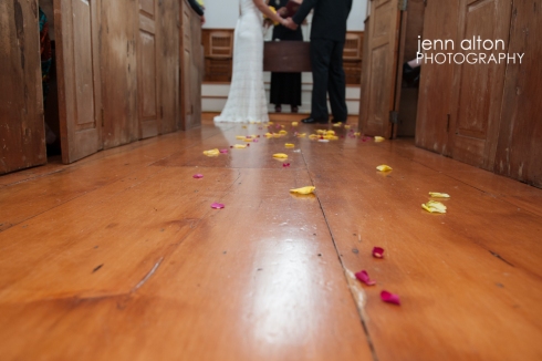 Bride and groom holding hands during ceremony and flower petals on the floor, Mashpee Old Indian Meeting House